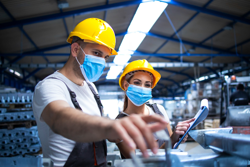 industrial workers with face masks protected against corona virus discussing about metal parts in factory Biogestion Services